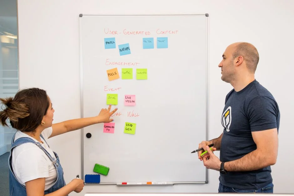 Two coworkers exchange ideas at a whiteboard during a creative strategy meeting.